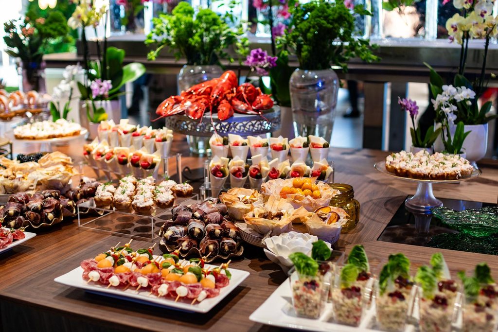 A catering display of lobster, canapés, charcuterie cones and skewers arranged among orchids and greenery